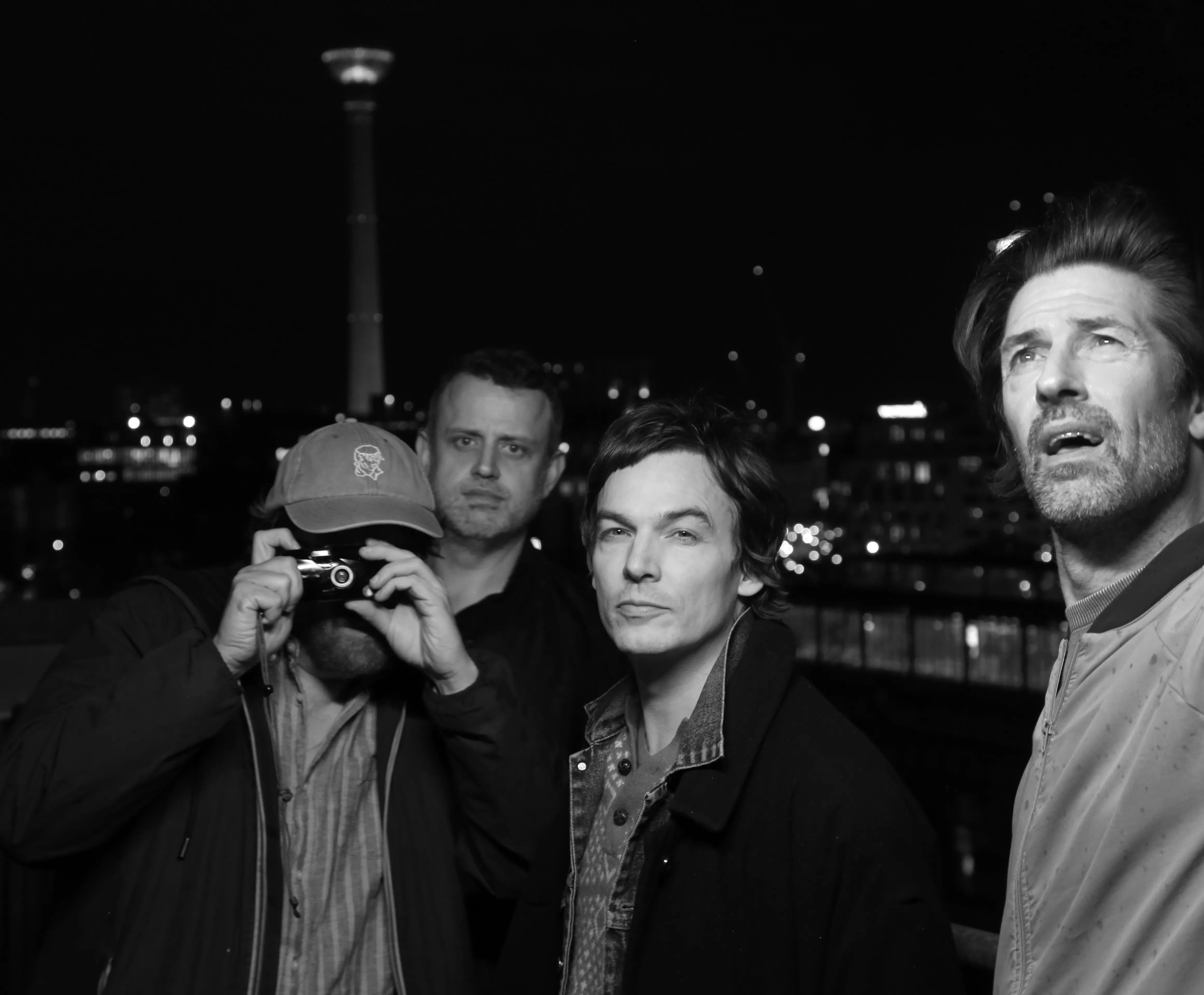 Aufnahme von vier Personen. Die linke hält eine Kamera vor das Gesicht.