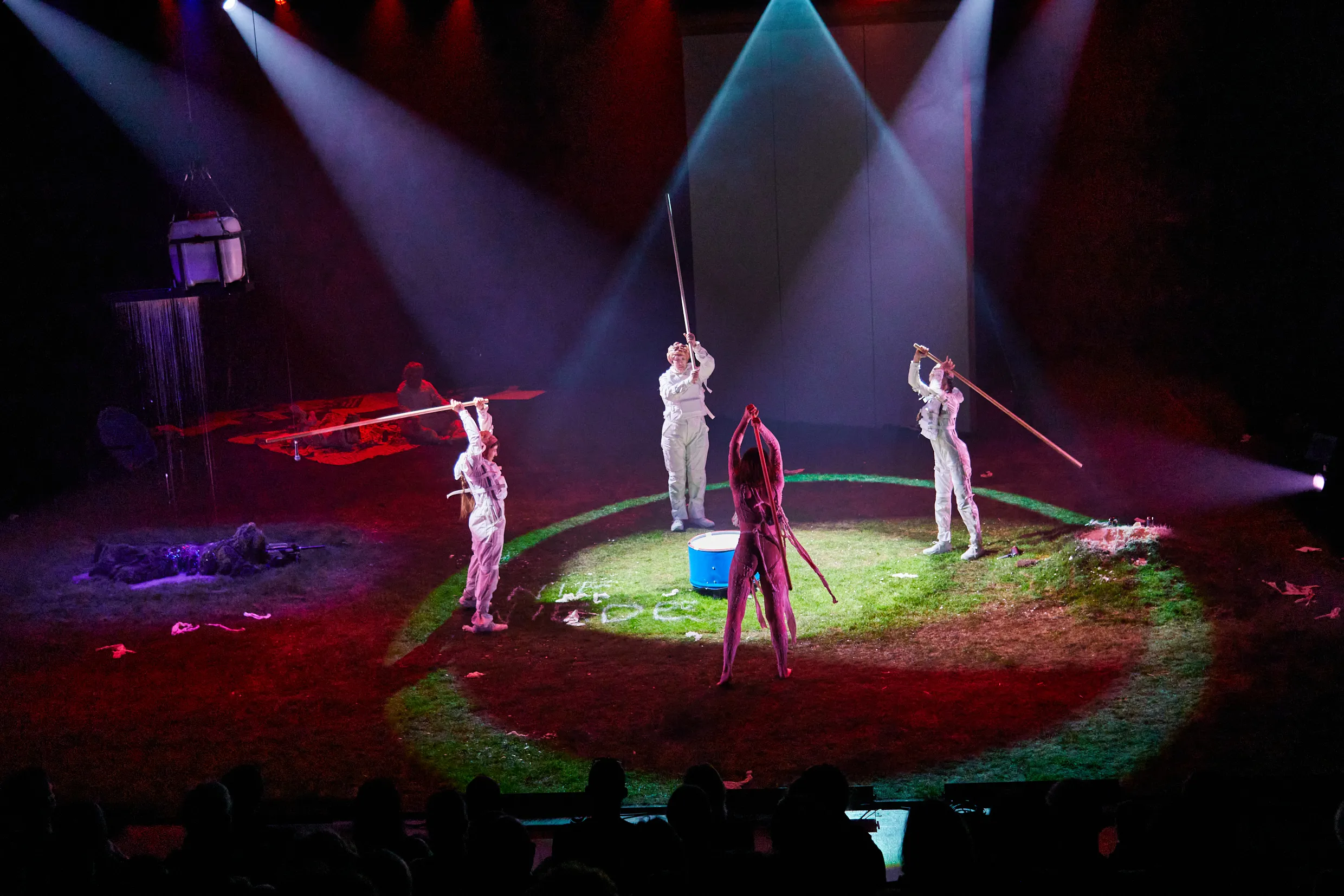 Vier Personen in weißen Anzügen stehen im Kreis und halten lange Stäbe in den Händen.