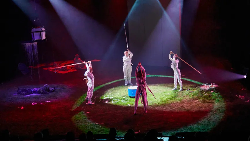 Vier Personen in weißen Anzügen stehen im Kreis und halten lange Stäbe in den Händen.