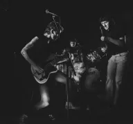 Drei Personen mit Schlagzeug und E-Gitarren.