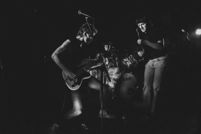 Drei Personen mit Schlagzeug und E-Gitarren.