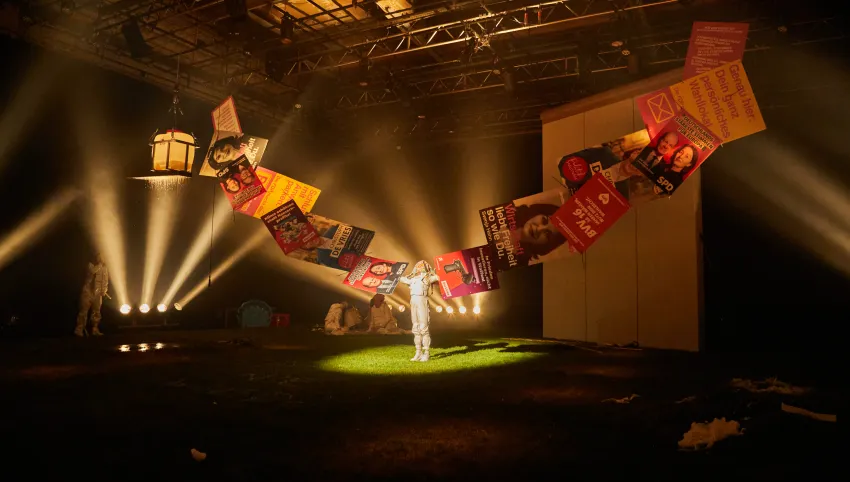 Eine Person streckt beide Arme zur Seite aus, die von aneinanderklebenden Wahlplakaten verlängert werden.
