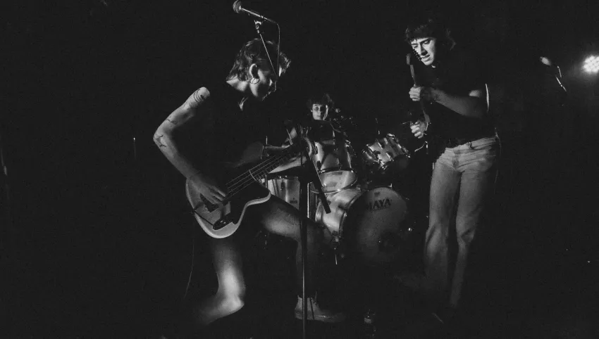 Drei Personen mit Schlagzeug und E-Gitarren.