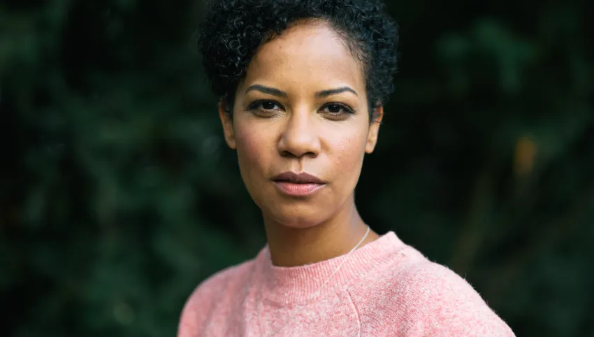 Porträtbild einer Person in einem rosa Pullover. Verschwommenes Grün im Hintergrund.