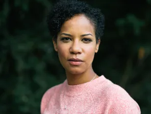 Porträtbild einer Person in einem rosa Pullover. Verschwommenes Grün im Hintergrund.