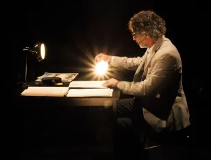 Eine Person sitzt an einem Tisch und leuchtet auf Papierblätter.