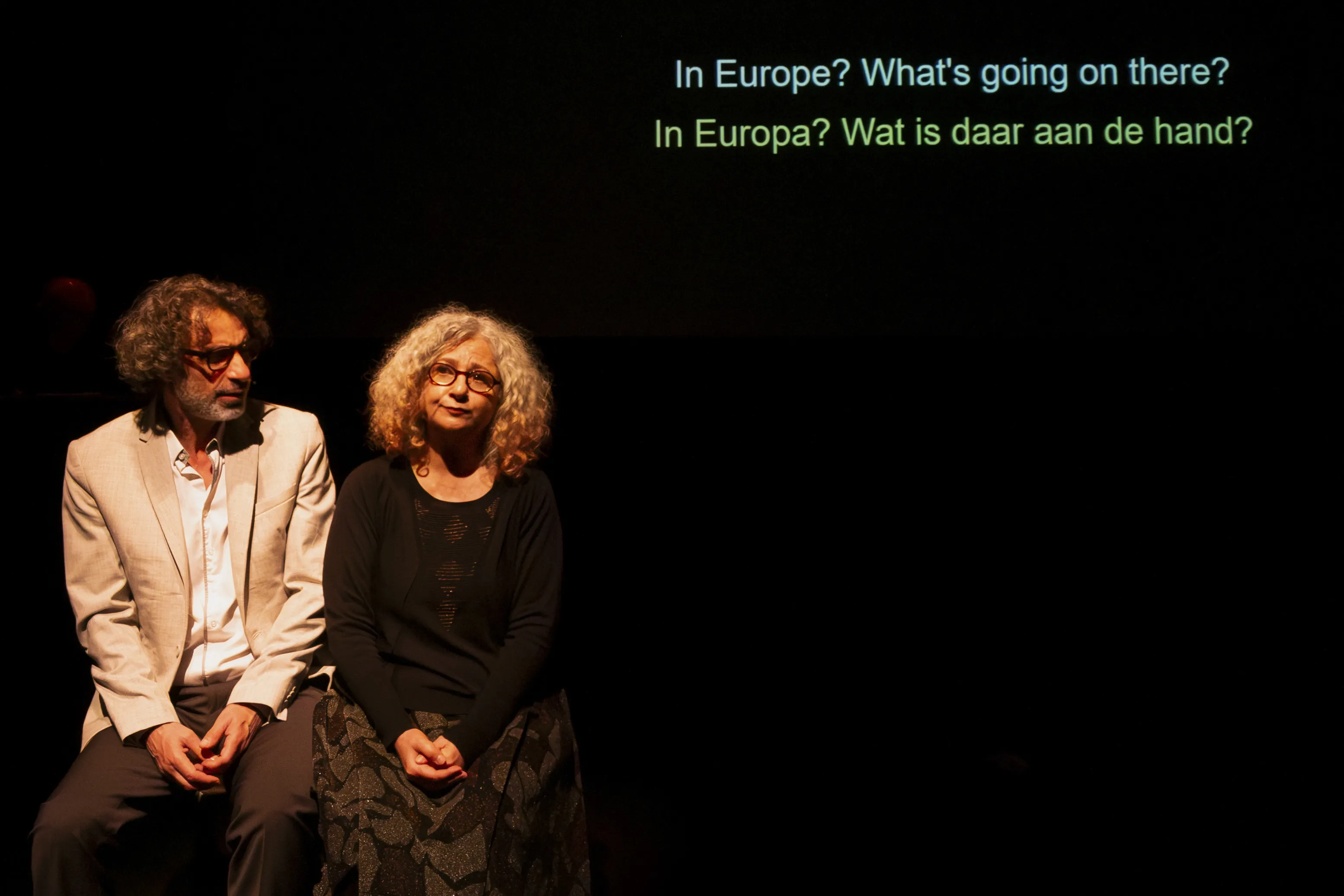 Zwei Personen sitzen nebeneiannder. Über ihnen der Text „In Europe? What’s going on there? In Europa? Wat is daar aan de hand?”