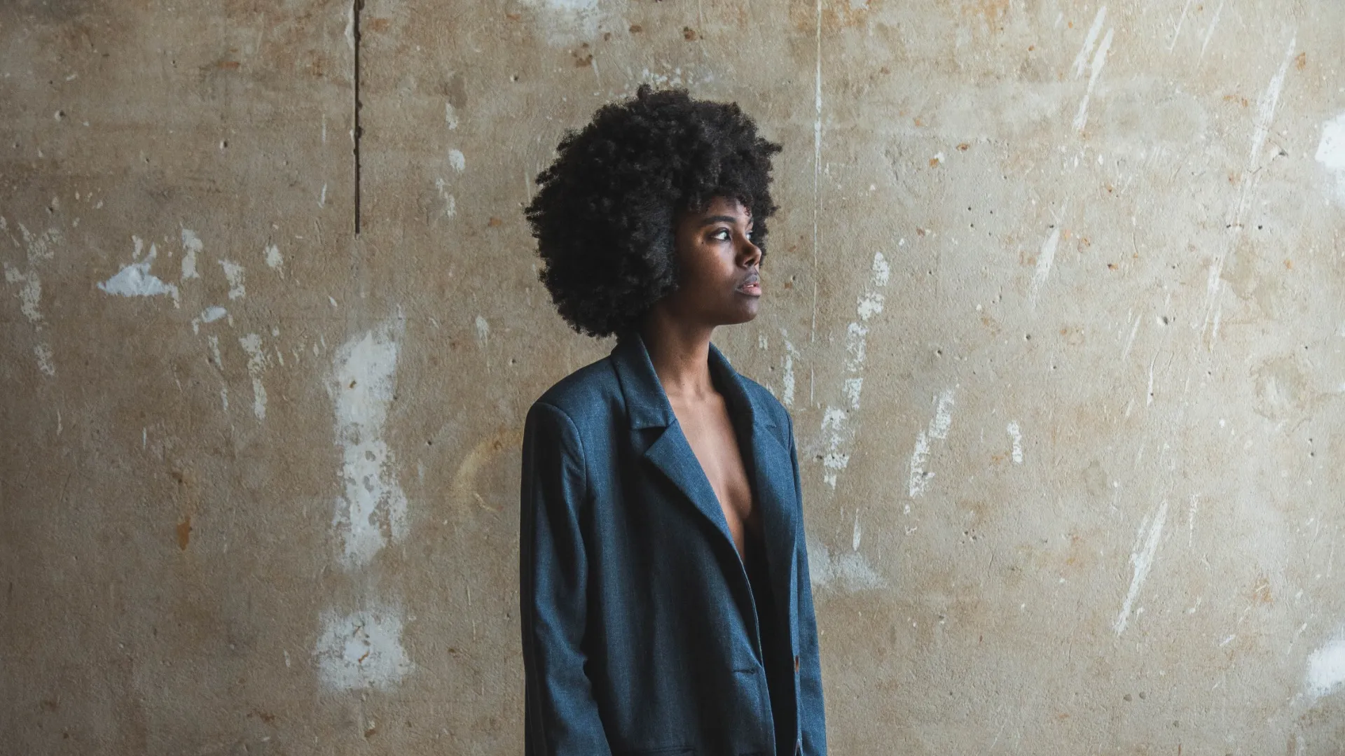 Eine Person trägt einen dunkelblauen Blazer und steht vor einer hellen Wand.