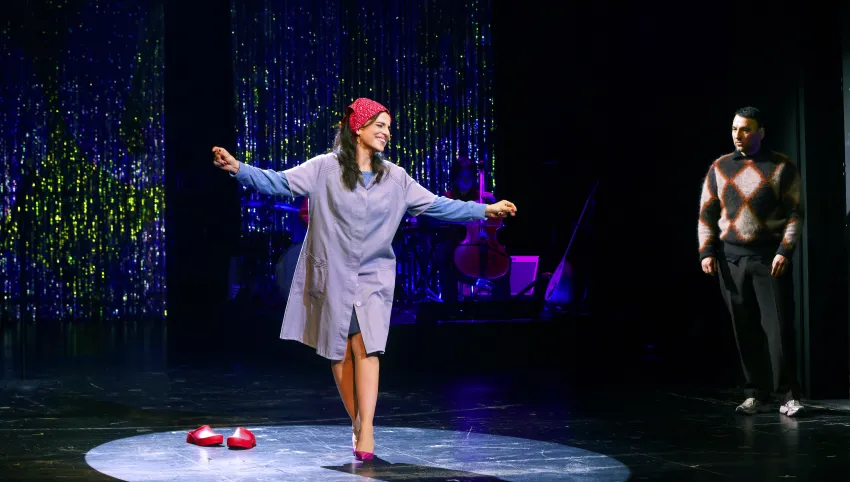 Eine Frau mit roter Kopfbedeckung und ausgestreckten Armen. Neben ihr ein Mann.