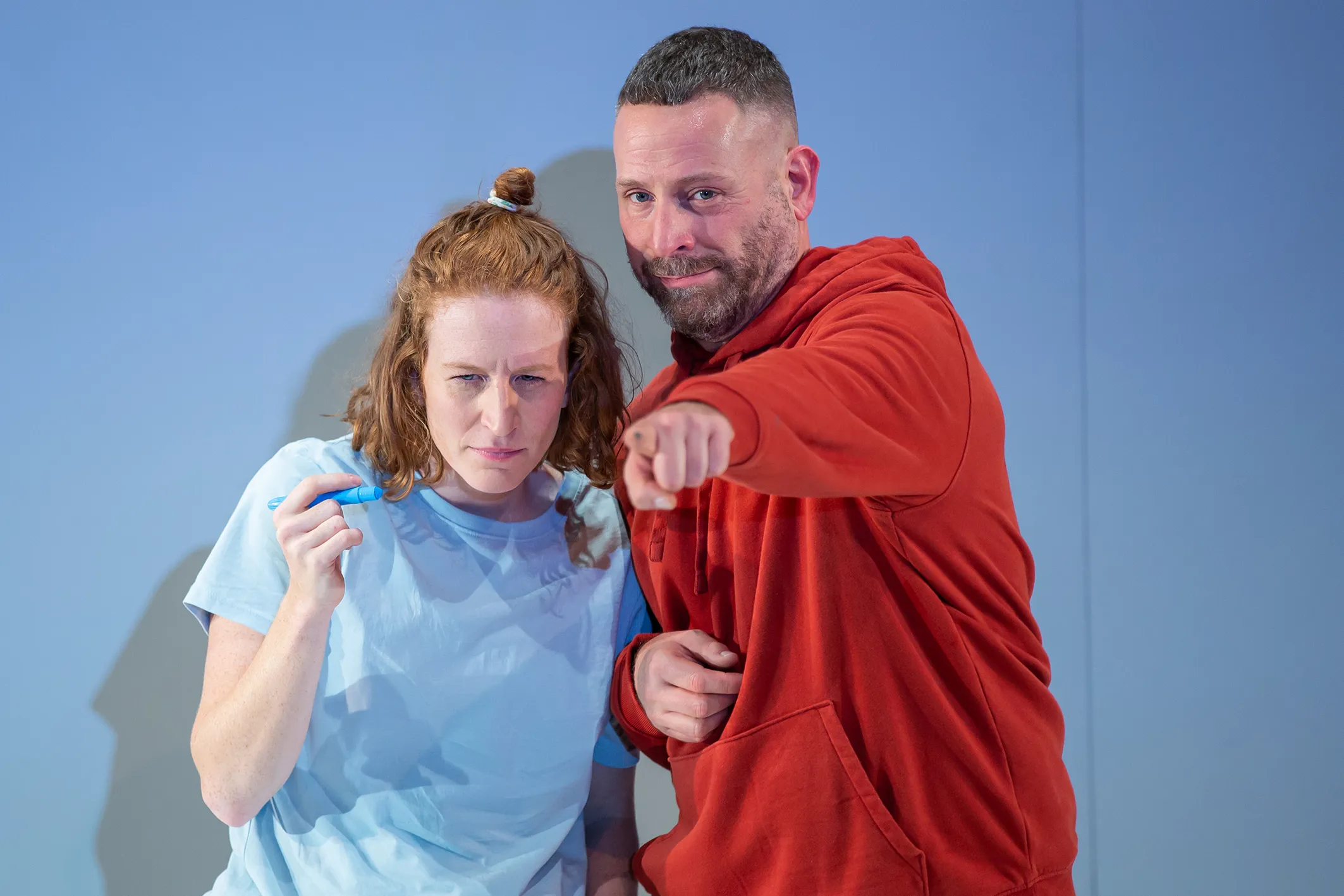 Eine Person trägt ein hellblaues Oberteil, eine andere einen roten Kapuzenpullover und zeigt mit ausgestrecktem Arm nach vorne.
