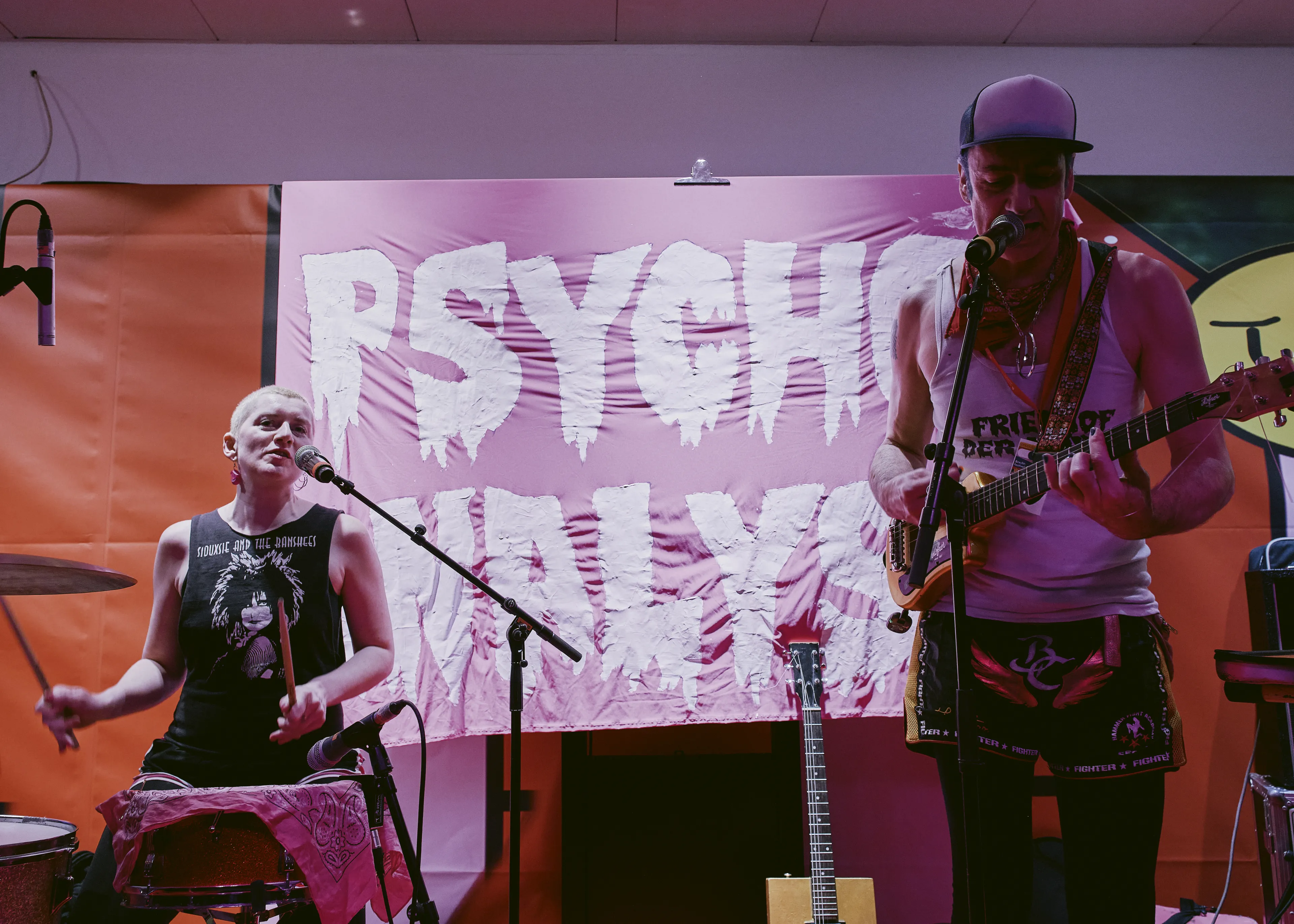 Brezel Göring, ein hochgewachsener Mann mit Baseballcap und Ukulele singt ins Mikro. Rechts hinter ihm  eine Person in schwarzem Achselshirt an den Percussions. Im Hintergrund aufgespannt: ein pinkes Tuch mit der Aufschrift "Psycho-Analyse". In weißen triefenden Großbuchstaben