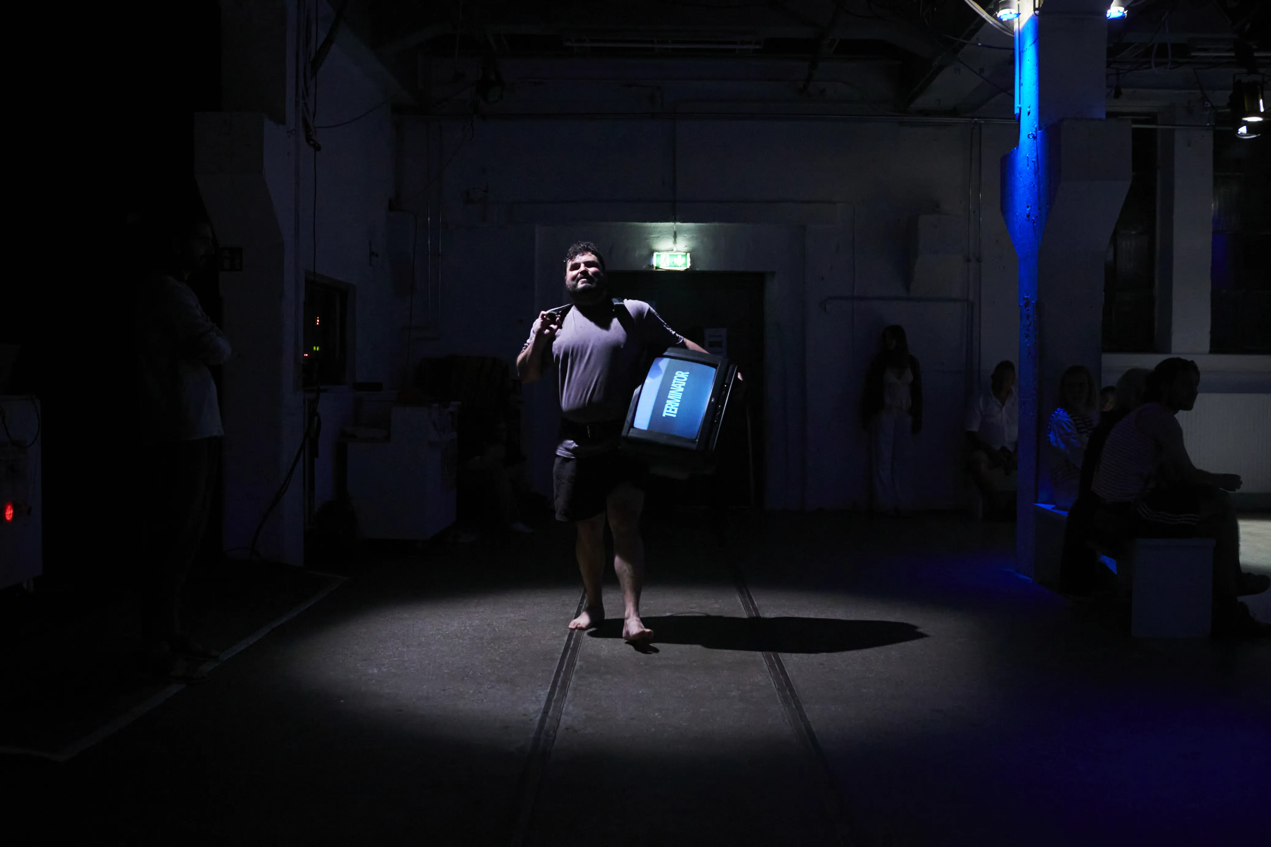 Eine Person, die einen Fernseher an der Hüfte trägt und barfuß durch einen Raum läuft.