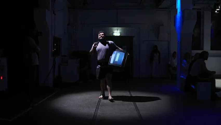 Eine Person, die einen Fernseher an der Hüfte trägt und barfuß durch einen Raum läuft.