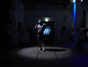 Eine Person, die einen Fernseher an der Hüfte trägt und barfuß durch einen Raum läuft.