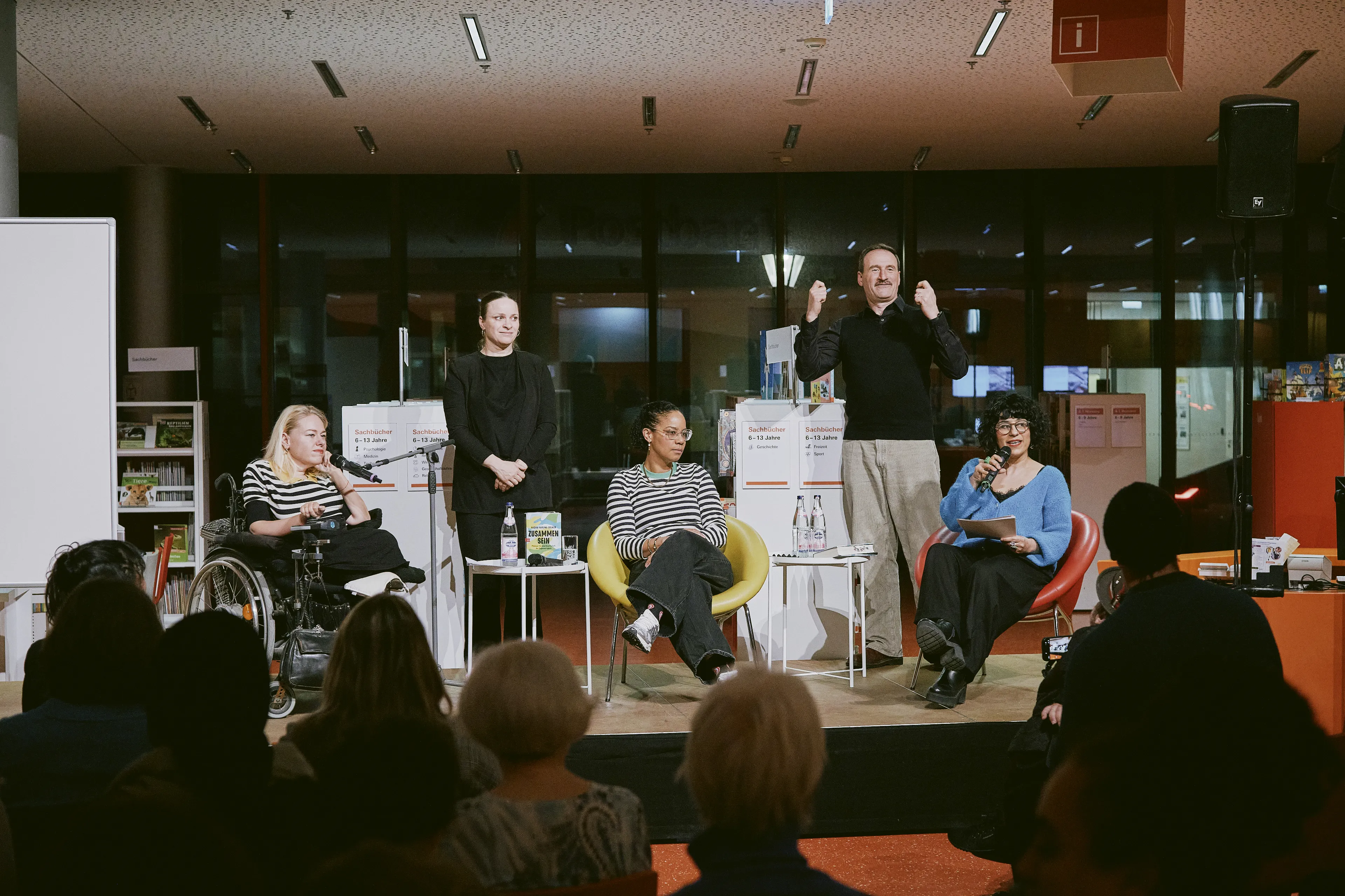 Ein Podium mit drei Frauen im Gespräch. Zwischen Ihnen steht ein Gebärdensprachendolmetscher und eine Gebärdensprachendolmetscherin