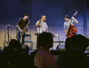 Momentaufnahme des Auftritts von O'Chavo Pretzlie bei der Brechtnacht. Ein Saxophonist, ein Sänger, ein Kontrabassist
