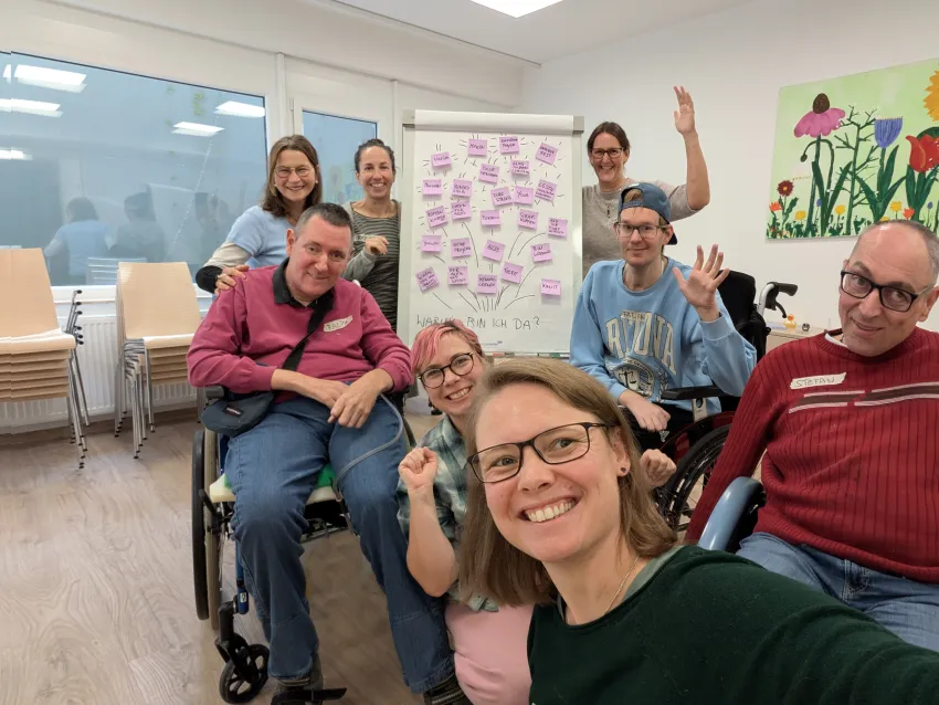 Ein Selfie von lachenden Personen, die sich um eine Papier-Leinwand mit Post-Its befinden.