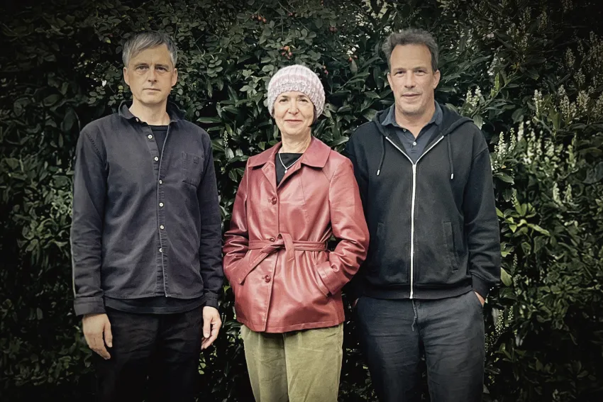 Drei nebeneinanderstehende Personen, Pflanzen im Hintergrund.