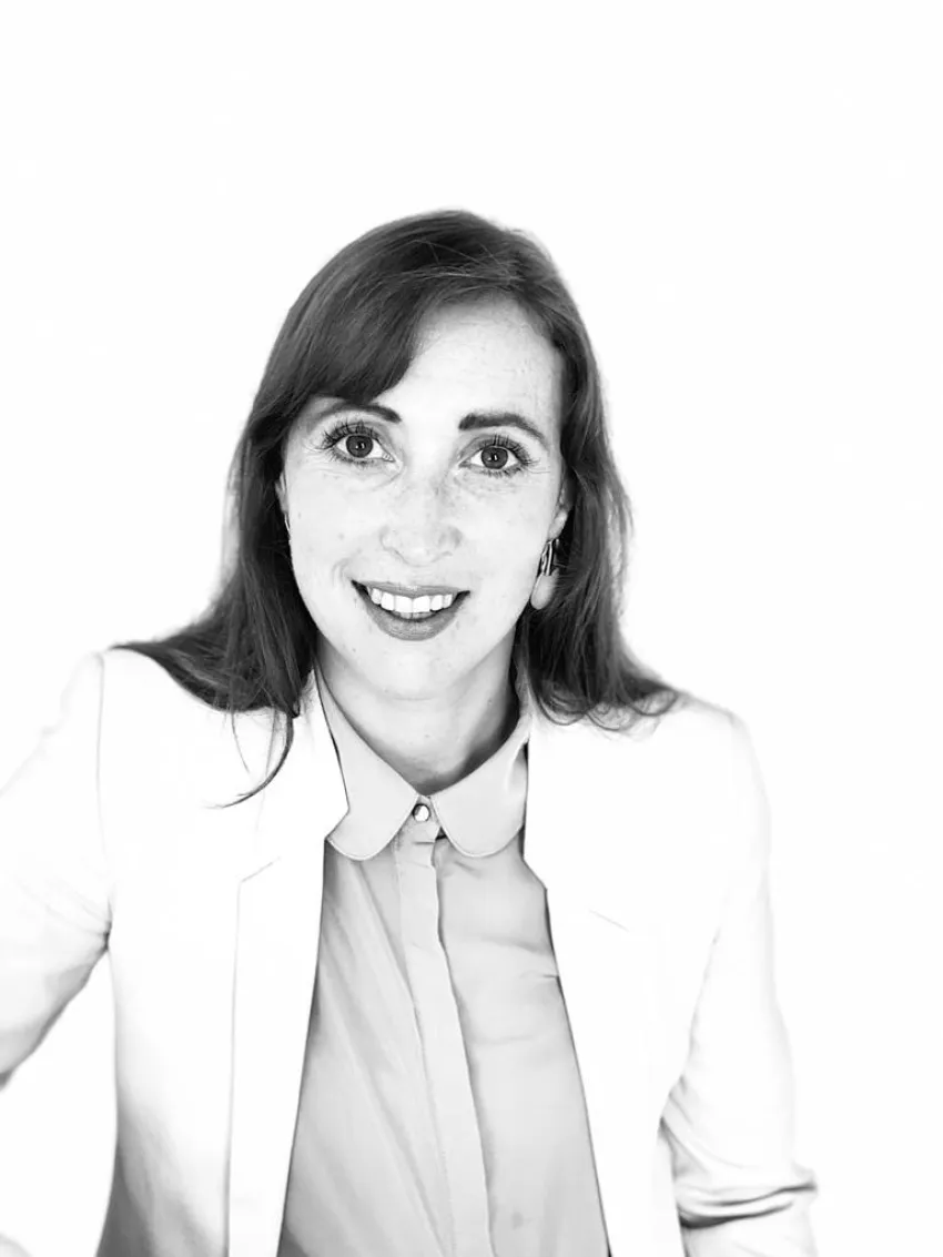 Schwarz-weißes Porträt einer lächelnden Person in hellem Blazer und Hemd.