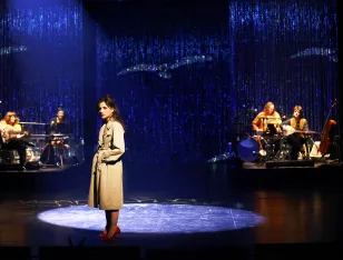 Eine Frau im beigen Mantel steht im Licht.