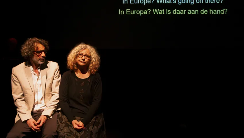 Zwei Personen sitzen nebeneiannder. Über ihnen der Text „In Europe? What’s going on there? In Europa? Wat is daar aan de hand?”