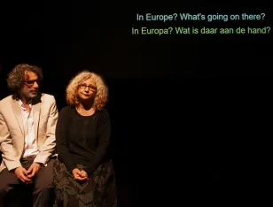 Zwei Personen sitzen nebeneiannder. Über ihnen der Text „In Europe? What’s going on there? In Europa? Wat is daar aan de hand?”