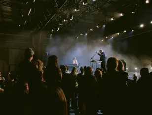 Momentaufnahme des Konzerts mit Sophia Kennedy auf der Bühne im martini-Park. Die Künstlerin steht mit einem Begleitmusiker im Bühnennebel. Davor gebanntes Publikum teils auf den aufsteigenden Rängen sitzend, teils stehend.