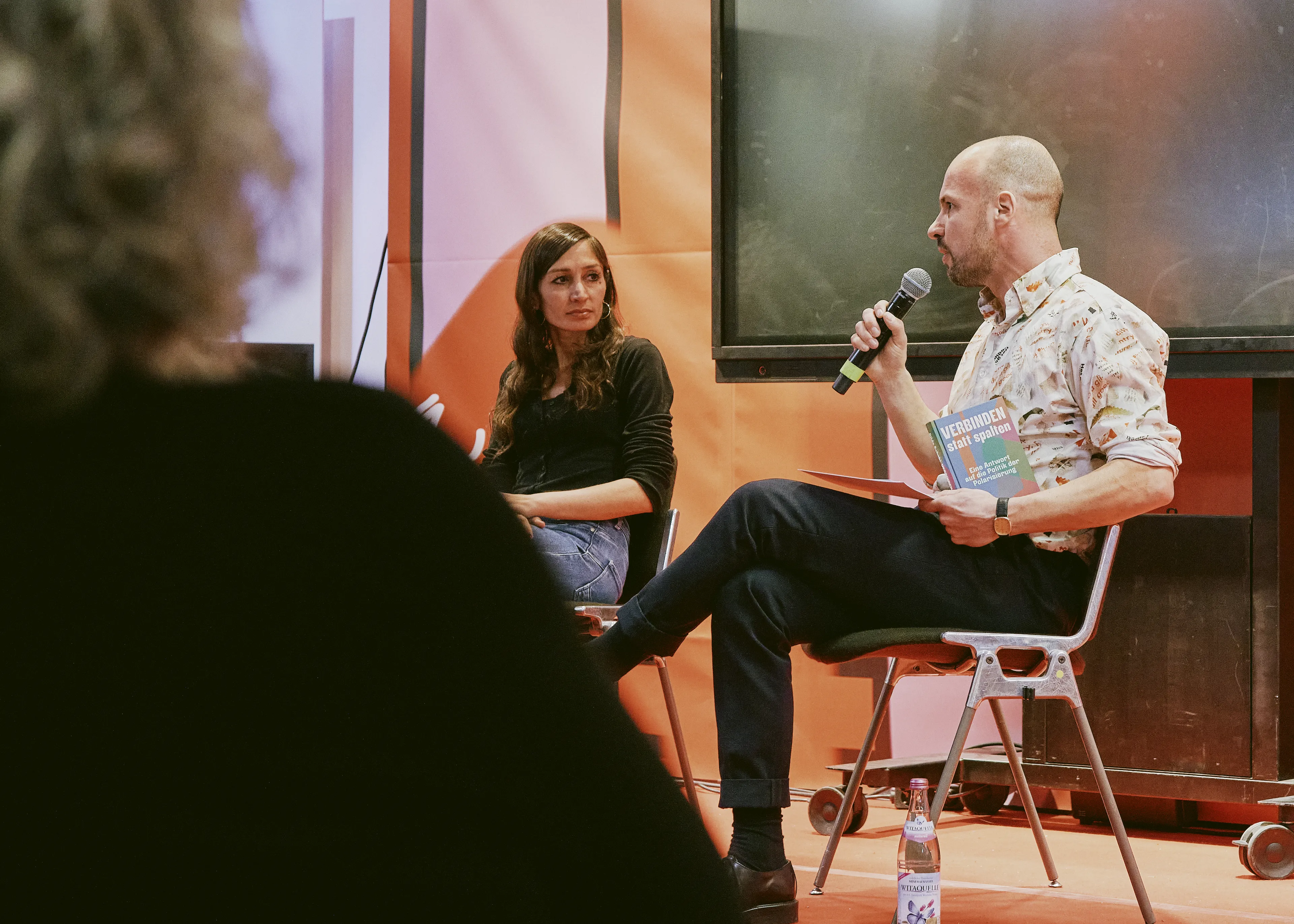 Der Moderator Martin Muth stellt der Autorin Gilda Sahebi im Rahmen der Lesung eine Frage.