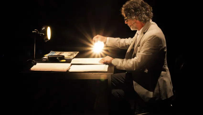 Eine Person sitzt an einem Tisch und leuchtet auf Papierblätter.