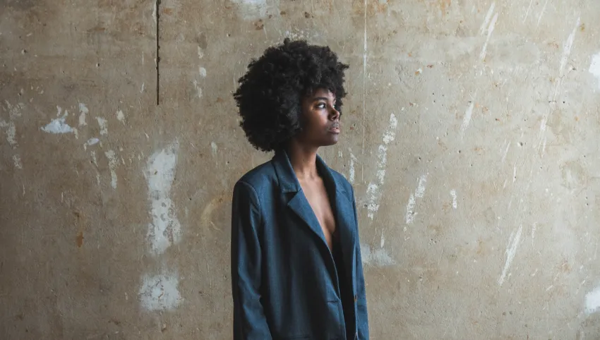 Eine Person trägt einen dunkelblauen Blazer und steht vor einer hellen Wand.