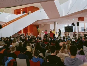 Im Foyer der Stadtbücherei Augsburg sind 150 Schüler versammelt. Der Brechtexperte Michael Friedrichs spricht auf dem Podium mit Sahar Rahami (Co-Festivalleitung), Jürgen Enninger (Kulturreferent) und Martina Wild (Bildungsreferentin) über die Bedeutung des Kreativwettbewerbs beim Brechtfestival