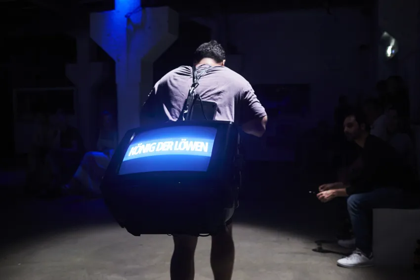 Eine Person trägt einen Fernseher mit „König der Löwen“ auf dem Rücken.
