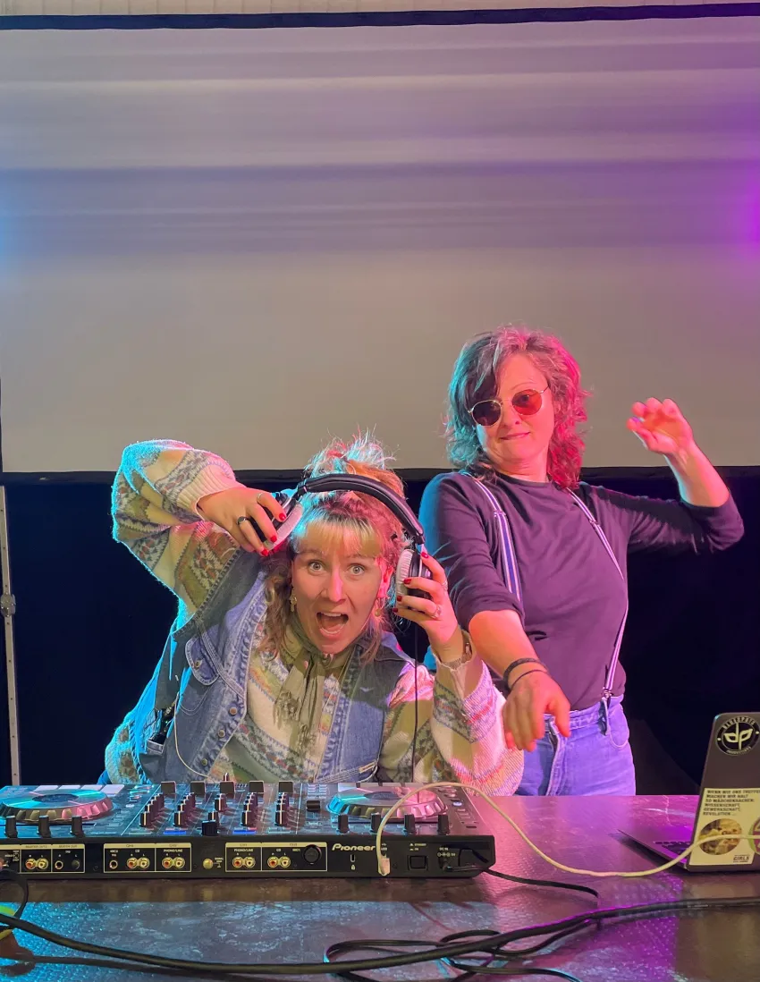 Eine Person mit Sonnenbrille und eine mit Kopfhörern vor einer DJ-Platte.
