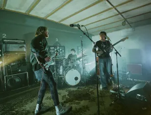 Im Vordergrund zwei Bandmitglieder mit Gitarre. Im Hintergrund ein Schlagzeuger.
